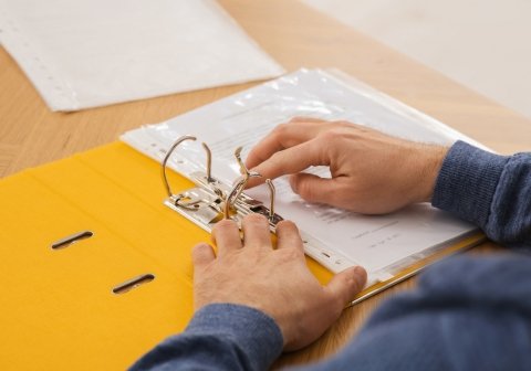 Man’s hands organizing papers in a folder – GDPR policy and documentation management.
