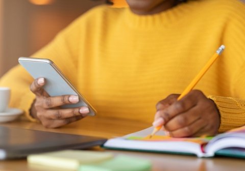 Woman taking notes with pencil and phone in hand – engaged in GDPR training session.