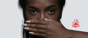 A woman covers her mouth with her hand, symbolizing forced silence. A red handprint with the word “STOP!” appears beside her, representing the fight against workplace harassment and the silencing of victims.