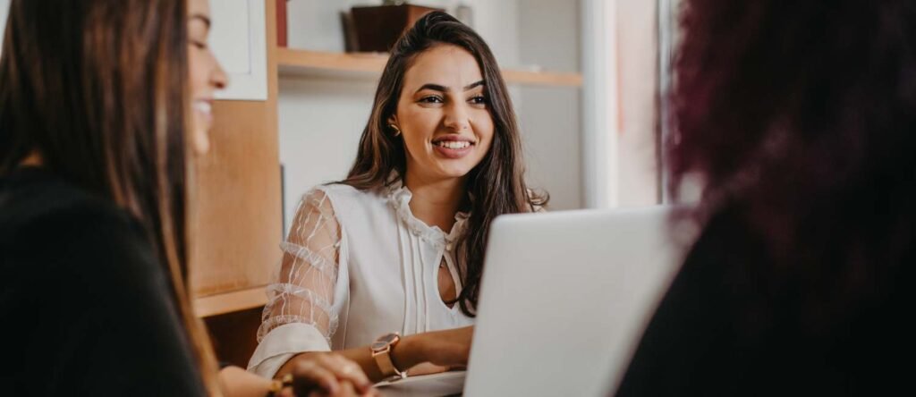 Three happy employees collaborating in an office setting, representing teamwork, engagement, and the benefits of strong HR and talent initiatives.
