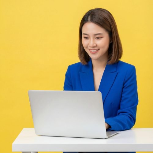 Professional woman in a blue blazer working on a laptop against a yellow background